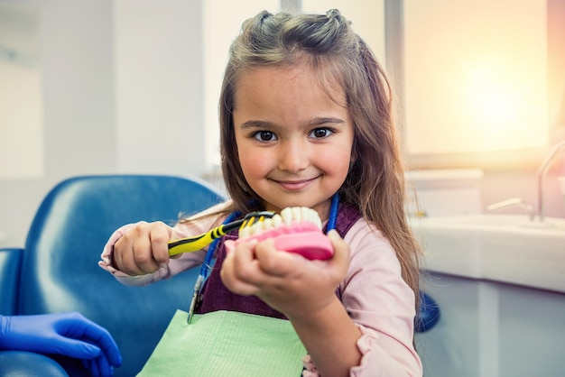 Hermosa niña sentada en una silla dental y sosteniendo una maqueta de dientes Concepto de diseño de dientes