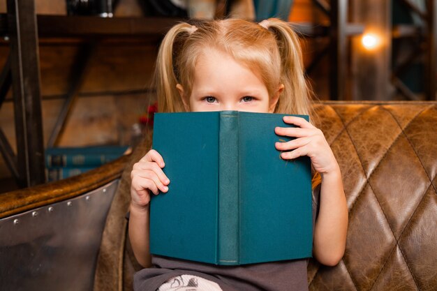 Hermosa niña sentada en el sofá con un libro