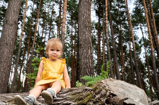 Hermosa niña sentada en un tronco en el bosque