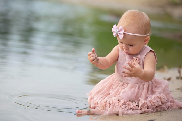 Una hermosa niña se sienta en la orilla del río y juega con arena y agua Niño y naturaleza