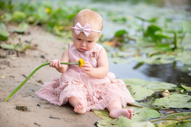 Una hermosa niña se sienta en la orilla del río y sostiene un lirio amarillo en sus manos.
