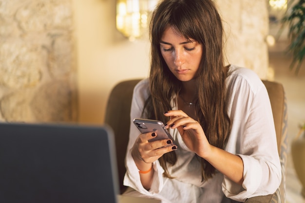 Una hermosa niña se sienta en un sillón y usa el teléfono