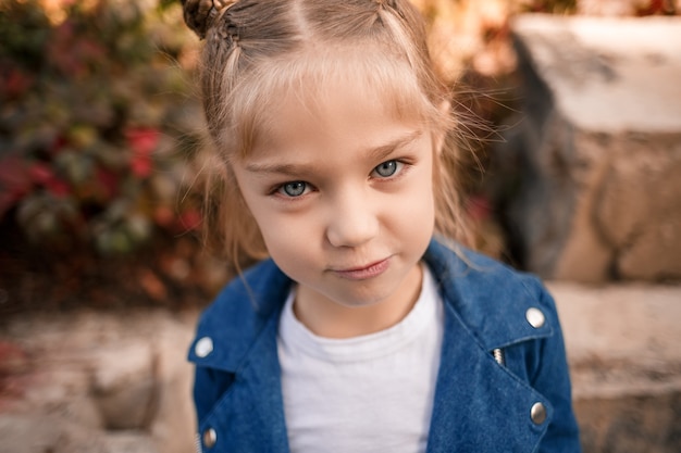 Una hermosa niña de unos siete años con una chaqueta de mezclilla mira a la cámara y hace muecas