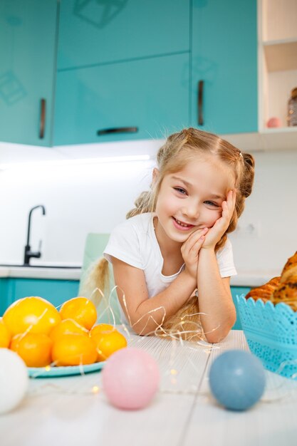 Hermosa niña de siete años. sentado a la mesa de la cocina. Vestido con una camiseta blanca. Felicidad y alegría en el rostro de un niño.