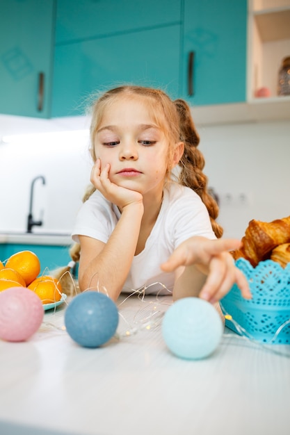 Hermosa niña de siete años. sentado a la mesa de la cocina. Vestido con una camiseta blanca. Felicidad y alegría en el rostro de un niño.