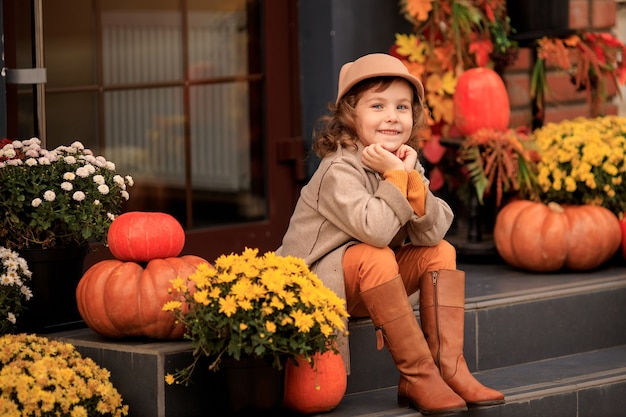 Hermosa niña con un sombrero en los escalones de la casa con calabazas y flores