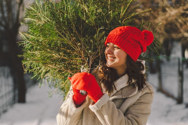 Una hermosa niña con un sombrero rojo lleva un árbol de Navidad Concepto de celebración de Navidad y Año Nuevo festivo de moda mínima