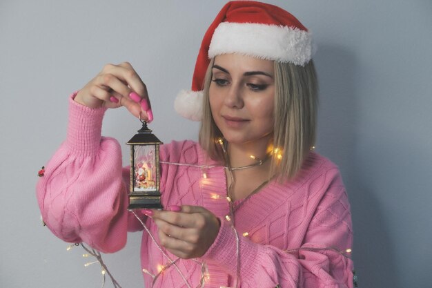 Una hermosa niña con un sombrero de Santa Claus decorado con linternas de año nuevo sostiene una linterna con cand