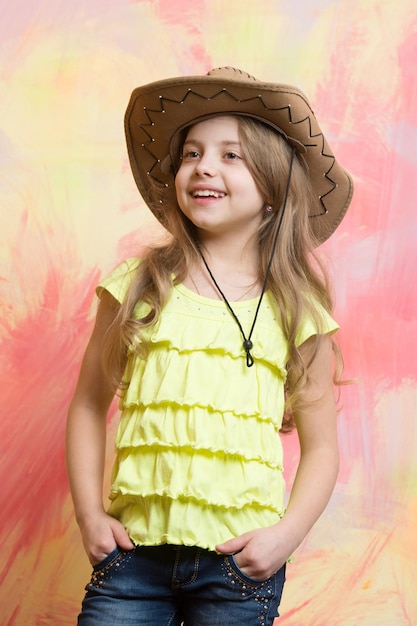 Hermosa niña con sombrero de vaquero de moda tiene una cara feliz sonriente sobre fondo de colores