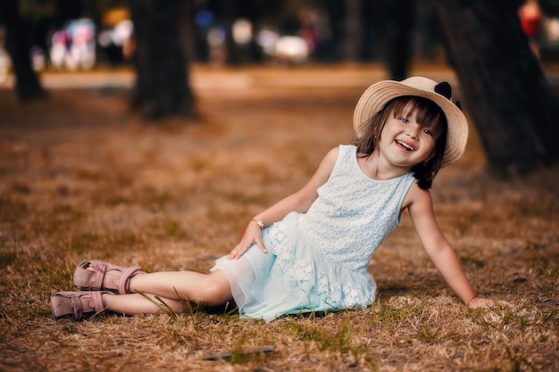 Hermosa niña en un sombrero y vestido blanco niña sentada en el césped