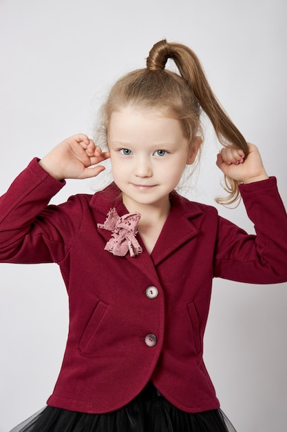 Hermosa niña sonríe, niño en ropa de otoño posa en una pared blanca