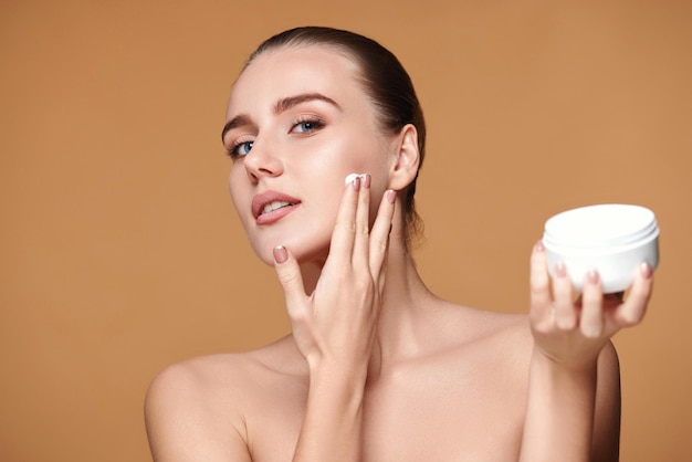 Hermosa niña sonriente aplicando crema para el cuidado de la piel en la cara