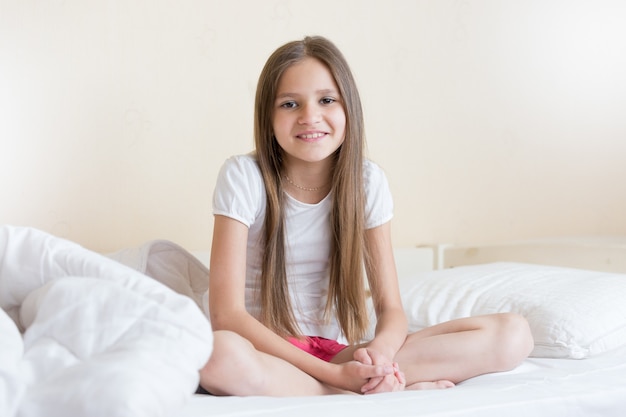 Hermosa niña sonriente con cabello largo oscuro sentada en la cama