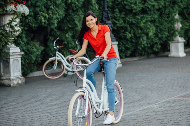 Hermosa niña sonriente en una camiseta roja monta una bicicleta blanca