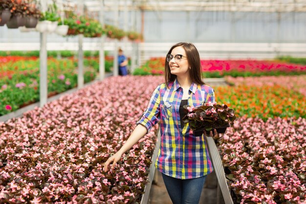 Hermosa niña sonriente en gafas, trabajador con flores en invernadero.