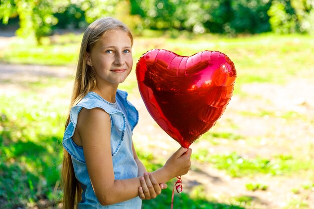 Hermosa niña sonriente con un globo en forma de corazón en la naturaleza