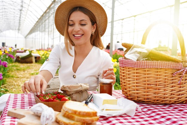 Hermosa niña sonriente haciendo un picnic Mujer joven toma una fresa Cosecha fresca y alimentos de kilómetro cero en el campo en primavera