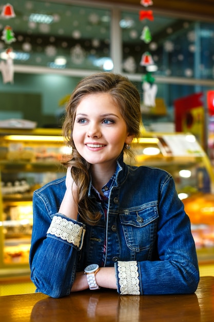 Hermosa niña sonriente con largo cabello rubio sentado en la cafetería