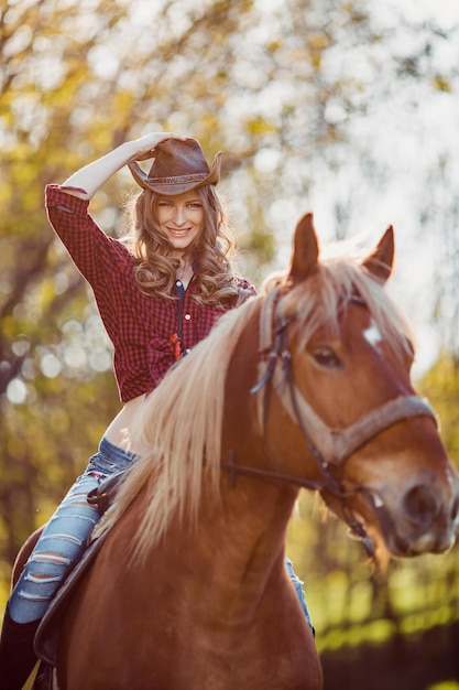 Foto hermosa niña sonriente montando a caballo en el campo de otoño