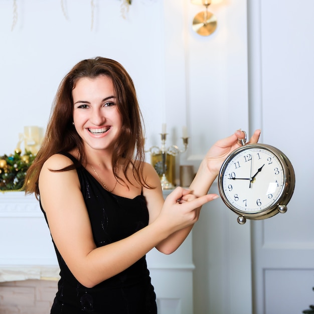 Hermosa niña sonriente se muestra en el reloj en el interior de Navidad