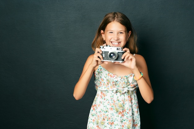 Hermosa niña sonriente (niña) con dientes blancos sosteniendo una cámara instantánea