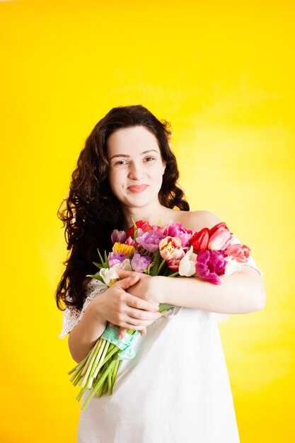 Hermosa niña sonriente de pie con ramo de tulipanes sobre fondo amarillo