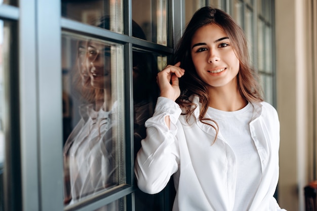 Hermosa niña sonriente posando bellamente cerca de la puerta de cristal