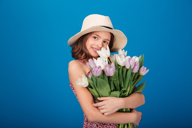 Una niña con un sombrero azul sostiene un ramo de tulipanes.