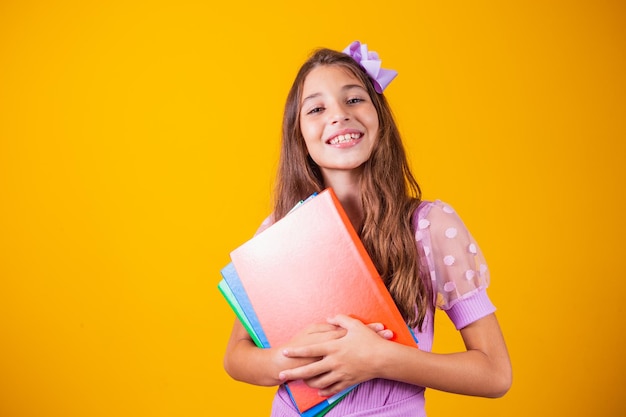 Foto hermosa niña sonriente sosteniendo libros que van a la escuela. retrato de cerca, fondo amarillo aislado, niñez. niño abrazando cuadernos. estilo de vida, interés, pasatiempo, tiempo libre, tiempo libre