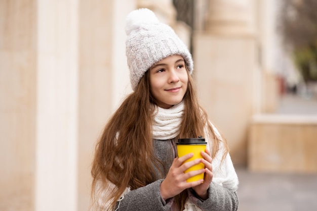 Una hermosa niña sonriente con una taza de café camina por la ciudad Atmósfera de otoño invierno