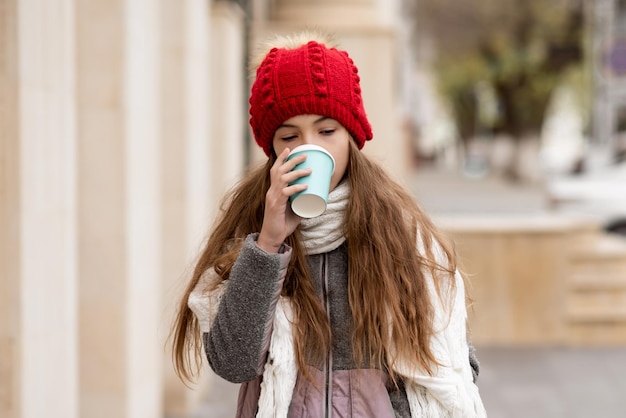 Una hermosa niña sonriente con una taza de café camina por la ciudad Atmósfera de otoño invierno
