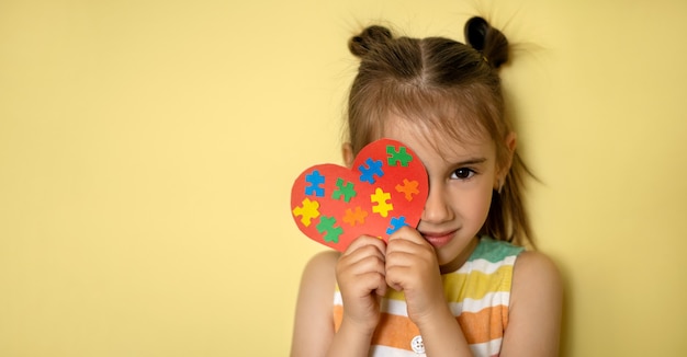 una hermosa niña sostiene un corazón con coloridos rompecabezas en sus manos cubriendo un ojo