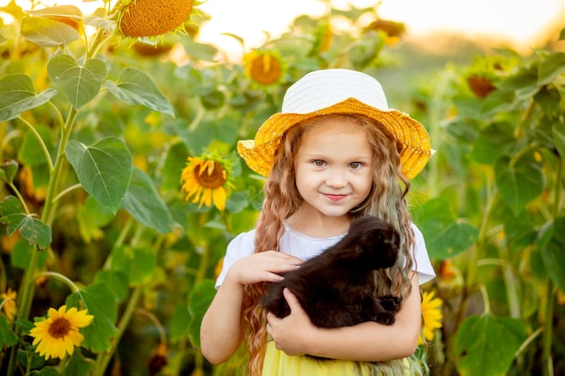 Hermosa niña sostiene un gatito negro en un campo con girasoles en verano