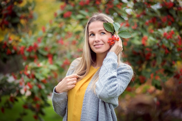 Hermosa niña sostiene una rama de bayas de viburnum cerca de su oreja