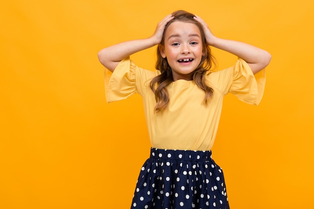 Hermosa niña sostiene su cabeza con las manos en una de una pared naranja, retrato emocional