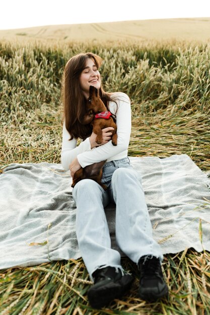 Una hermosa niña sostiene en sus brazos a un lindo perro salchicha con una venda roja alrededor del cuello. la anfitriona juega con una mascota en la naturaleza al atardecer.