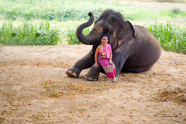 Una hermosa niña tailandesa vestida con el vestido tradicional del norte de Tailandia actúa y juega con un elefante para una sesión de fotos en un fondo borroso