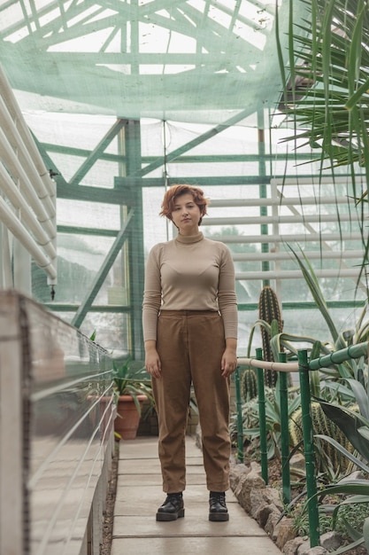 Una hermosa niña de talla grande de pie entre las plantas verdes del invernadero.