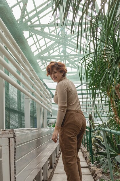 Una hermosa niña de talla grande de pie entre las plantas verdes del invernadero.