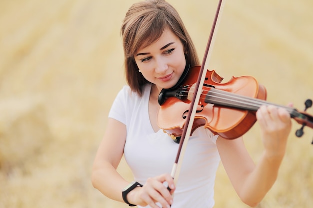 Hermosa niña tocando el violín en el campo