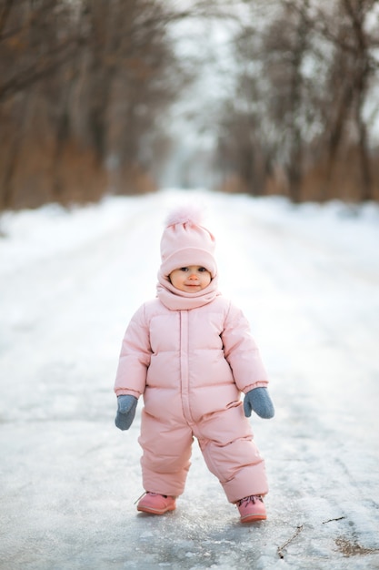 Hermosa niña en traje rosa en un parque nevado de invierno