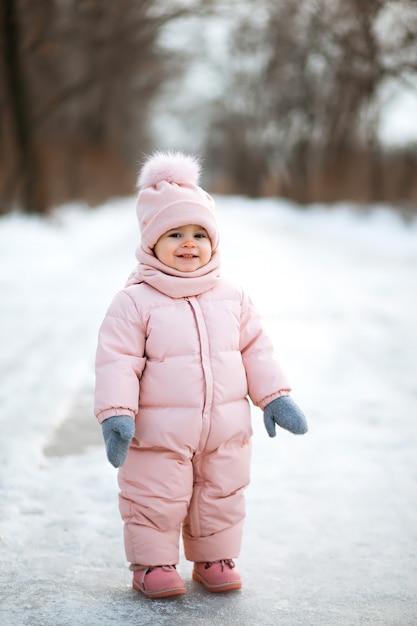 Hermosa niña en traje rosa en un parque nevado de invierno