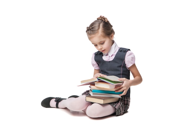 Hermosa niña en uniforme escolar con libros sentados en el suelo