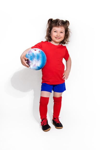 Hermosa niña en uniforme de fútbol y con balón en el brazo