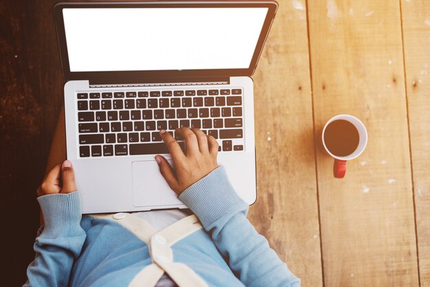 Hermosa niña usa laptop y taza de café en manos de la niña sentada en un piso de madera