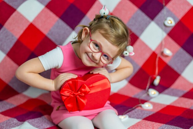 Hermosa niña en vasos con corazón de caja de regalo roja y globo. Día de San Valentín.