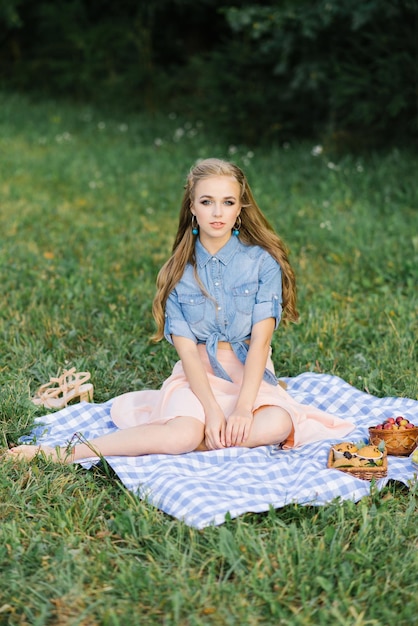 Una hermosa niña se ve feliz sentada en una manta con frutas que se encuentran en el fondo de la hierba