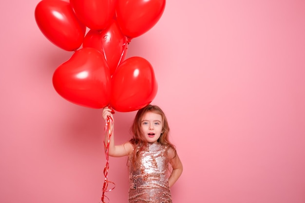 Hermosa niña vestida con lentejuelas con románticos globos de corazón rojo sobre fondo rosa