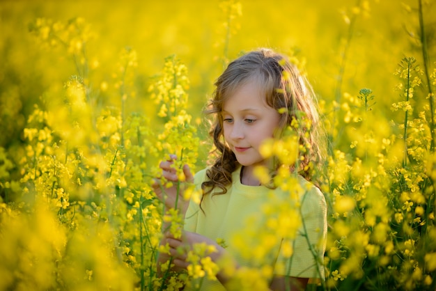 La hermosa niña en un vestido amarillo en el campo floreciente