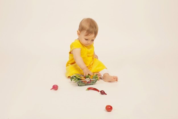 una hermosa niña con un vestido amarillo está sentada junto a una pequeña canasta con verduras